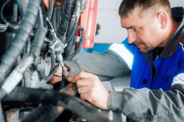 Mechanik samochodowy naprawia dużą ciężarówkę lub ciągnik w warsztacie Profesjonalny mechanik naprawia silnik ciężarówki Prawdziwy pracownik