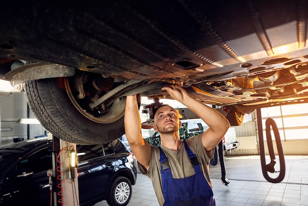 Mechanik samochodowy sprawdzający podwozie samochodu na stacji obsługi Mężczyzna pracownik naprawiający problem z samochodem Koncepcja konserwacji pojazdu