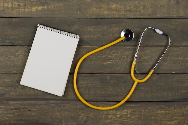 Medycyna i opieka zdrowotna koncepcja żółty stetoskop i pusty spiralny notatnik na drewnianym tle