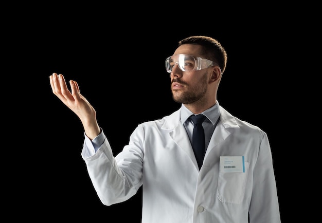 medycyna, nauka, opieka zdrowotna i koncepcja ludzi - mężczyzna lekarz lub naukowiec w białym płaszczu i okularach ochronnych dotykający czegoś niewidzialnego na czarnym tle