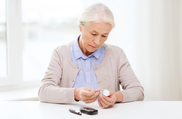 medycyna, wiek, cukrzyca, opieka zdrowotna i koncepcja ludzi - starsza kobieta z glukometrem i paskami testowymi sprawdzającymi poziom cukru we krwi w domu