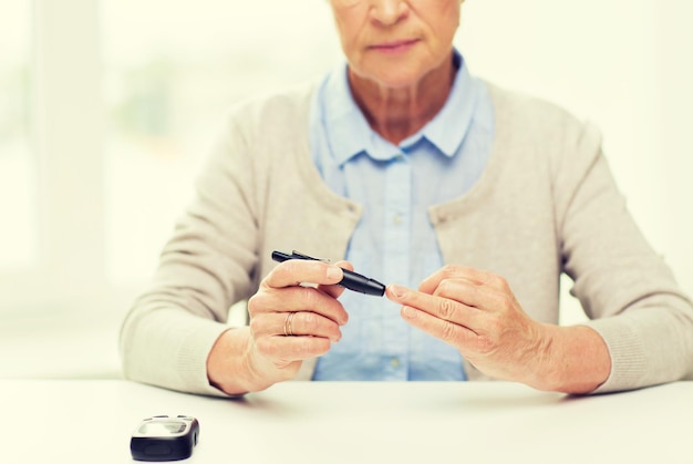 medycyna, wiek, cukrzyca, opieka zdrowotna i koncepcja ludzi - zbliżenie starszej kobiety z glukometrem sprawdzającym poziom cukru we krwi w domu