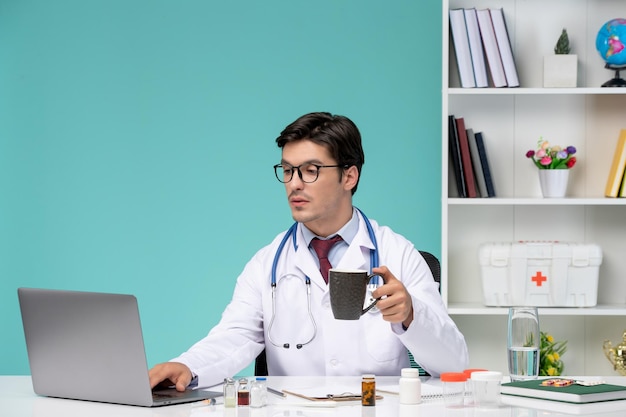 Medyczny Inteligentny Młody Lekarz W Fartuchu Laboratoryjnym Pracujący Zdalnie Na Komputerze Pijący Kawę