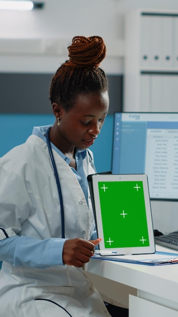 Medyk wskazujący na tablet z zielonym ekranem i rozmawiający z pacjentem w celu konsultacji. Lekarz i kobieta z technologią patrząc na klucz chrominancji z izolowanym tłem i szablonem makiety