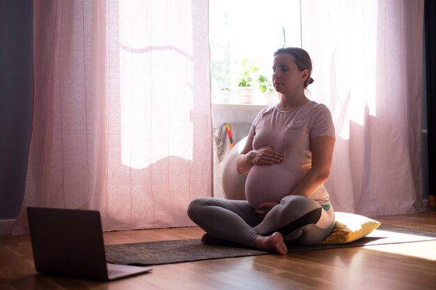 Medytacja jogi w ciąży. Pełnej długości zdrowa kobieta w ciąży robi ćwiczenia jogi w domu.