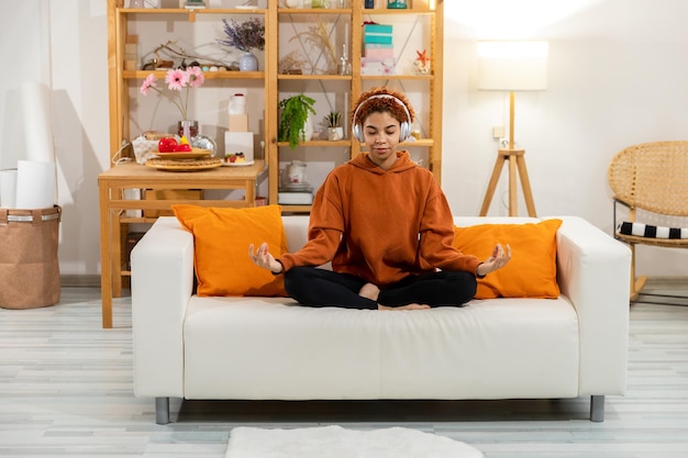 Medytacja uważności jogi Młoda zdrowa afrykańska dziewczyna ćwicząca jogę w domu Kobieta siedzi w pozie lotosu na macie do jogi medytując uśmiechnięty relaks w pomieszczeniu Dziewczyna robi ćwiczenia oddechowe joga w domu