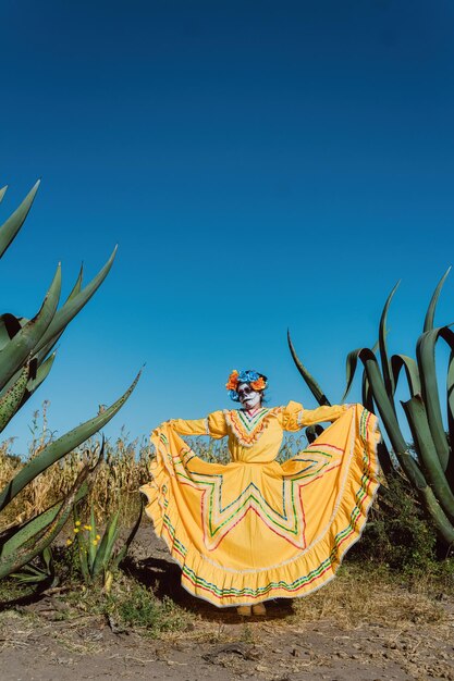 Meksykańska kobieta w kolorowej sukience i makijażu czaszki w meksykańskim pustynnym kaktusie