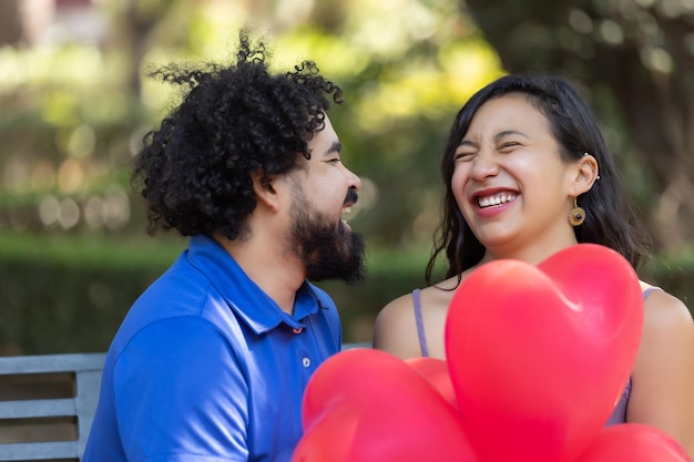 Meksykańska młoda para latynoska śmieje się i rozmawia w walentynki z czerwonymi balonami w kształcie serca