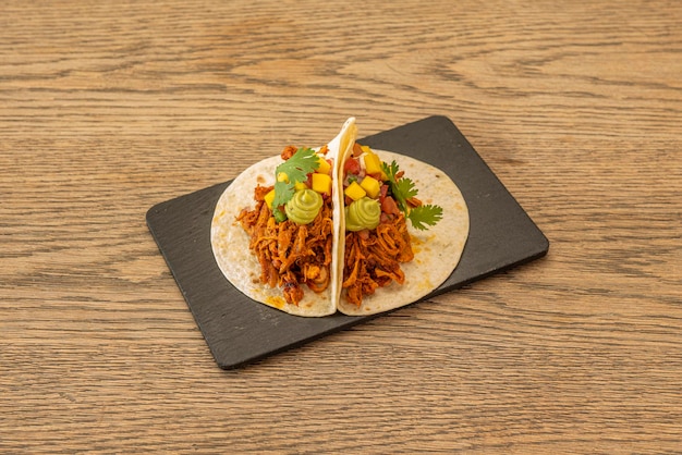 Meksykańskie tacos z pszennymi tortillami z kawałkami ananasa guacamole i szarpaną wieprzowiną na czarnym talerzu łupkowym