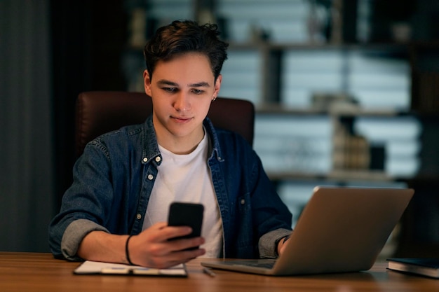 Menedżer młodego faceta pracujący w biurze przy użyciu laptopa i smartfona