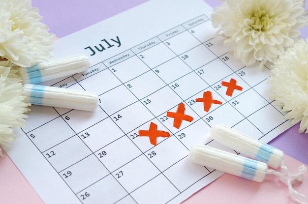 Zdjęcie menstrual tampons on menstruation period calendar with white flowers on lilac and pink background