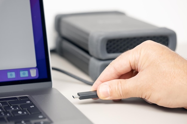 Zdjęcie męska ręka łącząca zewnętrzny dysk twardy z nowoczesnym laptopem na biurku