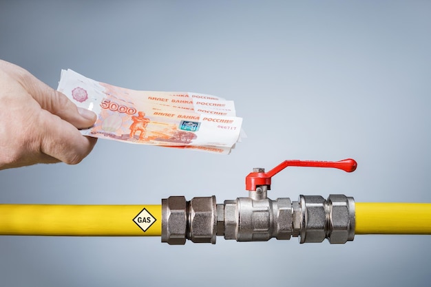 Męska ręka trzymająca rosyjskie banknoty pieniężne o wartości 5000 rubli i żółtą rurę gazową z zaworem sterującym Koncepcja dostawy gazu tylko w rublach