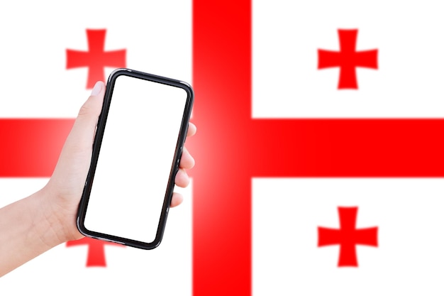 Męska ręka trzymająca smartfon z pustym ekranem na tle niewyraźnej flagi Gruzji Widok zbliżenia