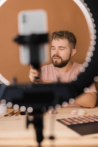 Męski bloger kosmetyczny z produktem do makijażu nagrywającym wideo w domu Za pomocą lampy pierścieniowej i smartfona Produkty kosmetyczne Vlog i koncepcja różnorodności