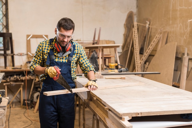 Zdjęcie męski cieśla ciie deskę z handsaw w warsztacie