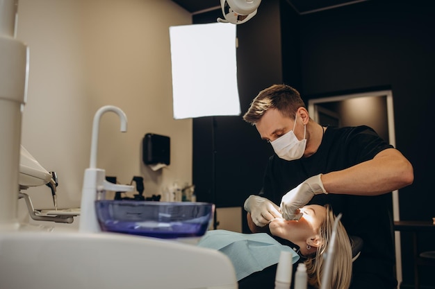 Męski dentysta w gabinecie dentystycznym rozmawia z pacjentką i przygotowuje ją do leczenia Wyjaśnienie procedury nowych implantów dentystycznych Widok z tyłu pacjenta koncentruje się na dentyście