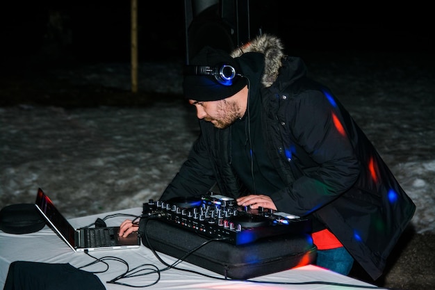 Męski DJ z brodą miksuje i gra słuchając piosenki na słuchawkach i korzystając z nowoczesnego sprzętu podczas imprezy w zimową noc