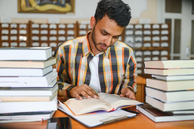 Męski indyjski uczeń przy biblioteką z książką