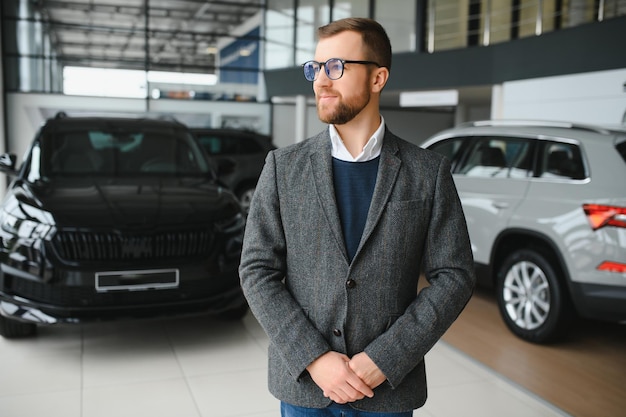 Męski klient kupujący mężczyzna w garniturze wybiera auto, aby odwrócić wzrok chce kupić nowy samochód w salonie samochodowym salon samochodowy salon dealerski sklep motoryzacyjny kryty koncepcja sprzedaży