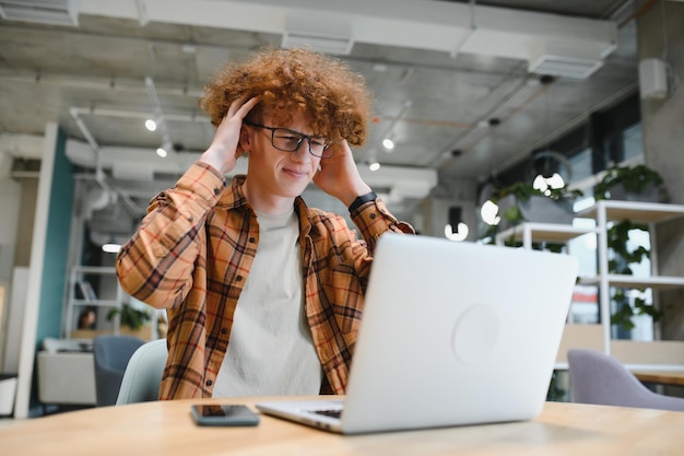 Męski programista nosi okulary chroniące oczy podczas pracy na freelance za pośrednictwem laptopasprytny student oglądający samouczek na netbooku