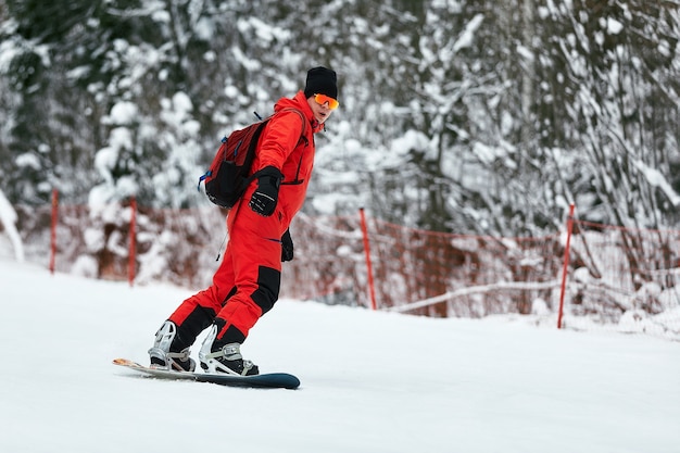 Męski snowboardzista w czerwonym garniturze jeździ na zaśnieżonym wzgórzu z koncepcją snowboardu, narciarstwa i snowboardu.