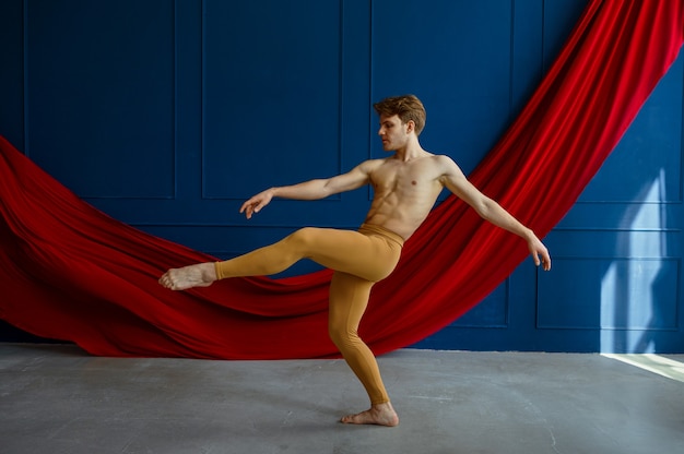 Męski tancerz baletowy, szkolący się w klasie tańca, niebieskie ściany i czerwone sukno. Wykonawca o muskularnym ciele, wdzięku i elegancji ruchów