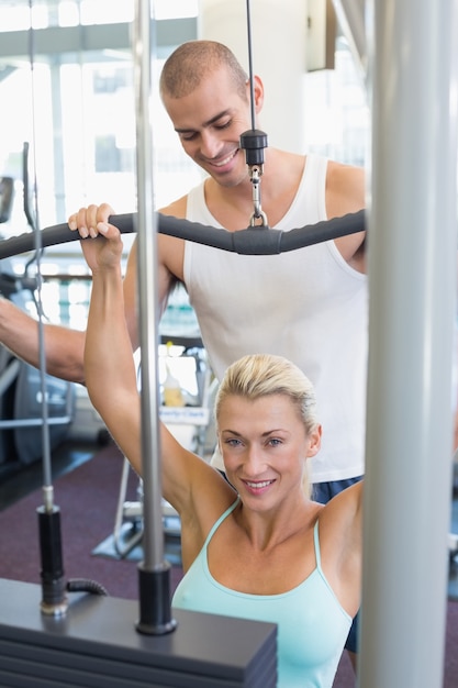 Męski trener pomaga kobiety na lat maszynie w gym