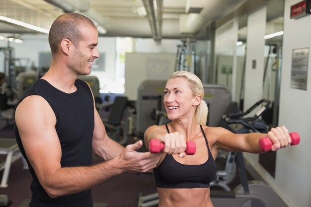 Męski trener pomaga kobiety z dumbbell w gym