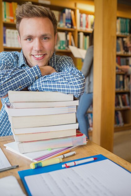 Męski uczeń z stertą książki podczas gdy inny w tle przy biblioteką