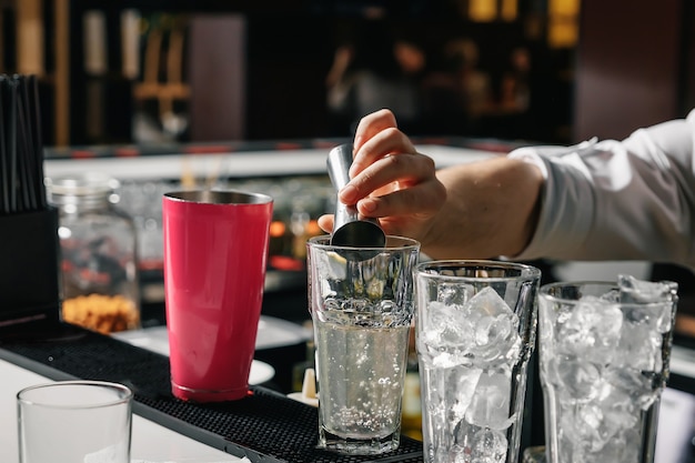 Męskie dłonie barmana, robi koktajl na barze, szklanki z lodem.