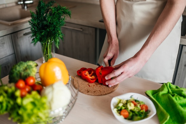 Męskie dłonie do krojenia sałatki i cebuli, gotowanie zdrowej żywności w kuchni.