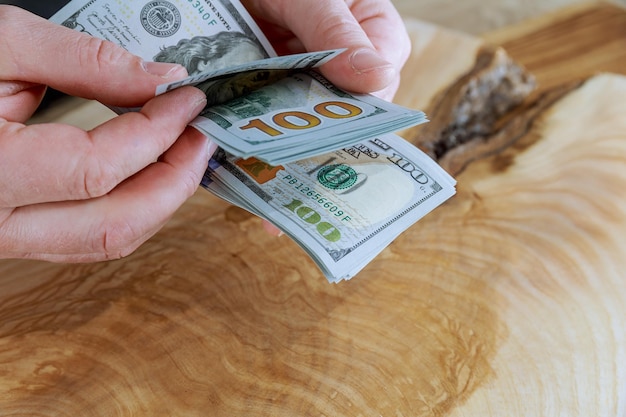 Męskie dłonie liczące stu dolarowe nad drewnianym stołem