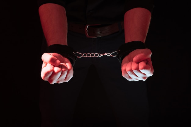 Męskie dłonie skute w skórzanych kajdankach do seksu BDSM za plecami. poddanie się i dominacja