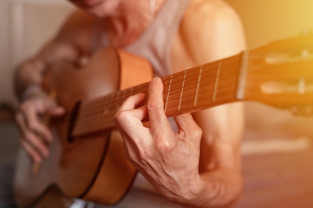 Męskie dłonie starszego starszego mężczyzny rasy kaukaskiej trzymającej i grającej na gitarze klasycznej z bliska w domu nieprofesjonalny gitarzysta bez twarzy ludzie grają amatorską muzykę domowe hobby i rozbłysk rekreacyjny