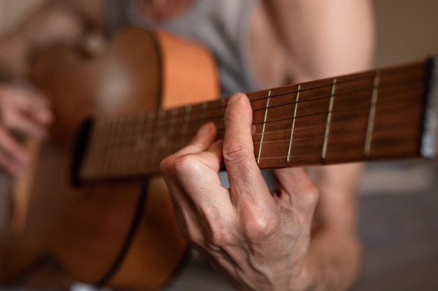 Męskie dłonie starszego starszego mężczyzny rasy kaukaskiej trzymającej i grającej na gitarze klasycznej z bliska w domu nieprofesjonalny gitarzysta bez twarzy ludzie grają amatorską muzykę domowe hobby i wypoczynek