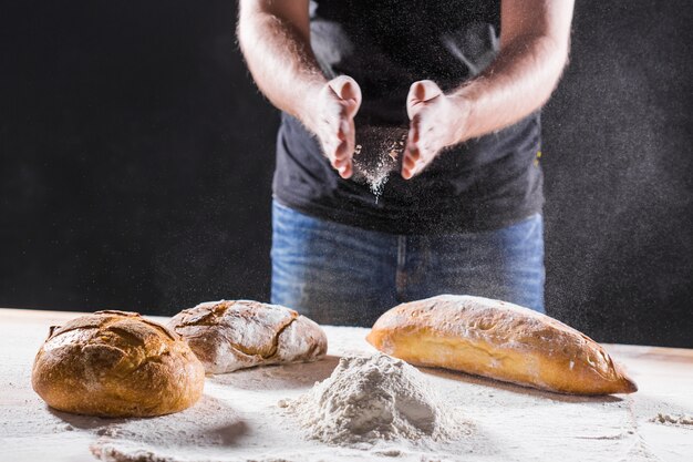 Męskie dłonie w mące i rustykalnym organicznym bochenku chleba