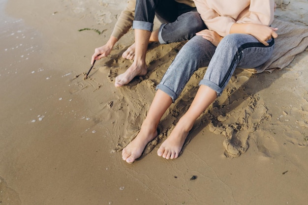 Męskie i kobiece nogi na plaży Facet rysuje na piasku Serce