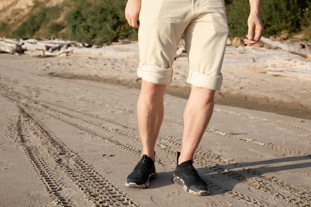 męskie nogi w beżowych szortach spacerujące po plaży