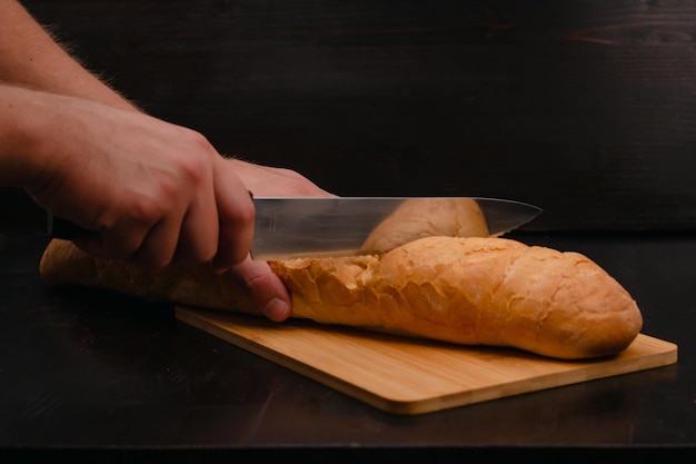 Męskie ręce kroją chleb na desce do krojenia na tle drewna