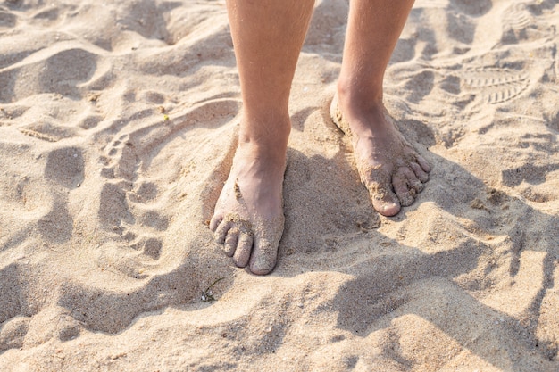 Męskie stopy w piasku. Spaceruj wzdłuż piaszczystej plaży w letni dzień. Podróż i turystyka.