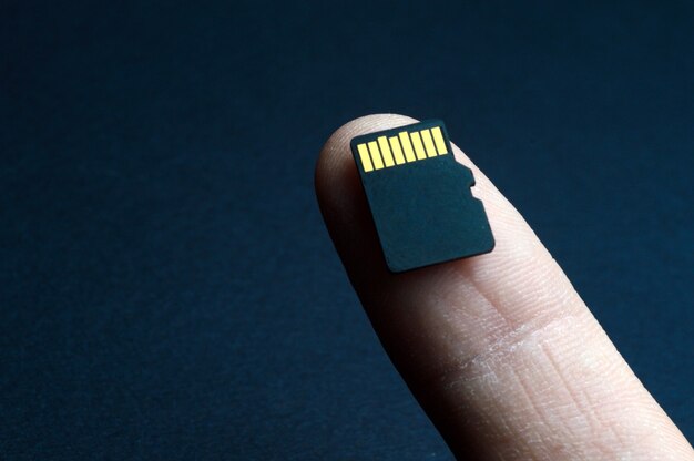 Męskiej ręki trzymającej kartę Micro SD na czarnym tle.