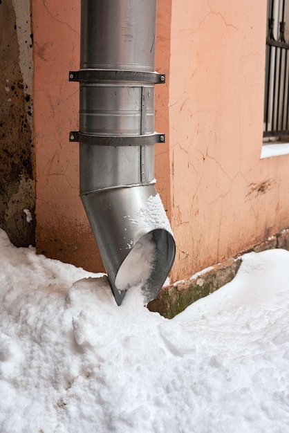 Metalowa fajka wodna na rogu domu jest wypełniona śniegiem
