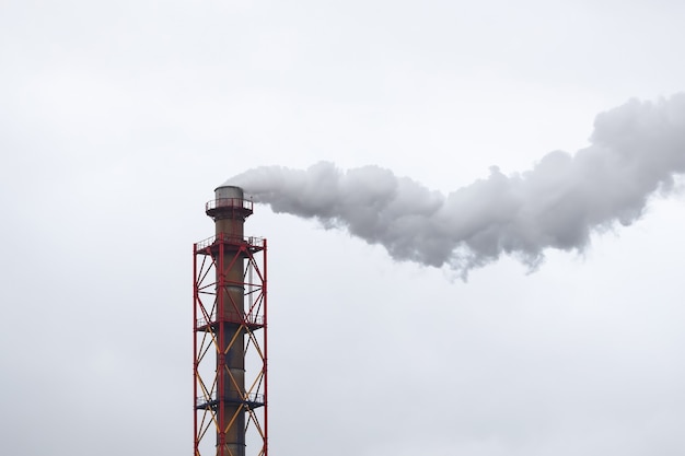 Metalowa fajka, z której na zachmurzone niebo wydobywa się biały dym