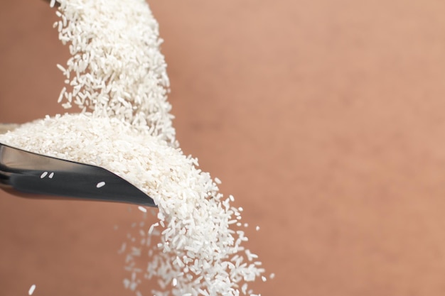 Metalowa łyżka z białym ryżem. Spadające ziarna ryżu. Skopiuj miejsce. Na białym tle na brązowym tle.
