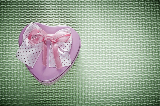 Metalowe różowe pudełko upominkowe w kształcie serca ze wstążką na zielonym tle koncepcji wakacji