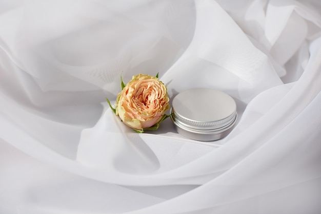 Metalowy okrągły pojemnik na słoik do pielęgnacji brwi z delikatną różą na białej scenie tekstylnej