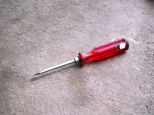 Metalowy śrubokręt z czerwonym uchwytem jest umieszczony na cementowej podłodze