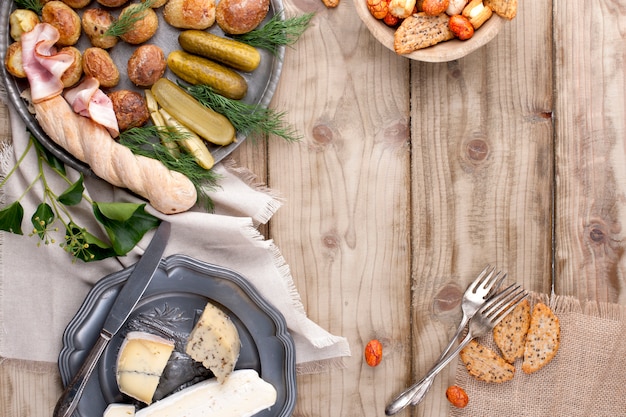 metalowy talerz z pieczonymi ziemniakami, ogórkami i zieleniną, sucharkami i serem na drewnianym stole