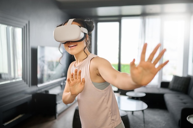 Metaverse i futurystyczny VR z kobietą w salonie swojego domu za pomocą zestawu słuchawkowego, aby uzyskać dostęp do gry 3D Technologia wirtualnej rzeczywistości i gier z kobietą-graczem używającym AI do grania w gry online